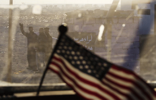 Iraqis wave behind a US flag on the dashboard of a Mine Resistant Ambush Protected (MRAP) vehicle, part of the last US military convoy to leave Iraq on December 18, 2011 near Nasiriyah, Iraq., From ImagesAttr