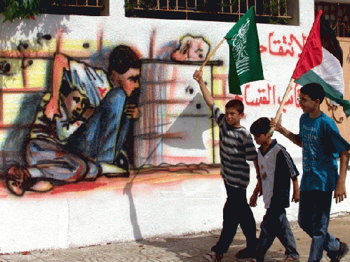 Palestinian boys carrying Hamas and Palestinian flags in the Gaza Strip walk past graffiti showing the death of 12-year old Mohammad al-Durra, who was shot dead during Israeli-Palestinian clashes, in this October 6, 2000 file photo., From ImagesAttr