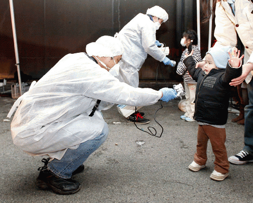 March 2011 Officials in protective gear check for signs of radiation on childre who are from the evacuation area near th