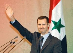 Syrian President Bashar al-Assad in front of a poster of his father, Hafez al-Assad.