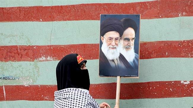 An Iranian woman displays the images of Leader of the Islamic Revolution Ayatollah Seyyed Ali Khamenei and Founder of the Islamic Republic Ayatollah Ruhollah Khomeini outside the wall of the former U.S. Embassy in Tehran. (File photo)