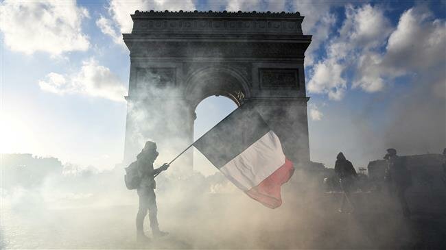 In this file photo taken on March 16, 2019, a protester holds a French national flag as he walks among the tear gas smoke past the Arc de Triomphe on the Place de l'Etoile in Paris. (Photo by AFP)