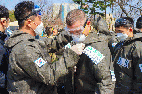 South Korean Army Soldier assists a U.S. Army soldier in donning protective equipment before sanitizing a COVID-19 infected area during a joint disinfecting operation in Daegu, South Korea, March 13, 2020.